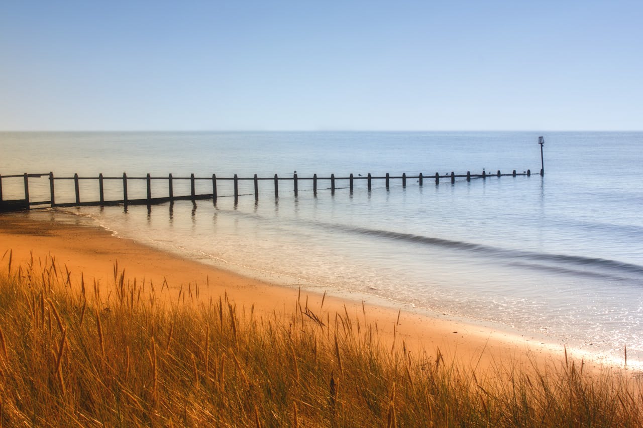 Home Tranquil coastal scene with golden sand, calm sea, and clear blue sky.