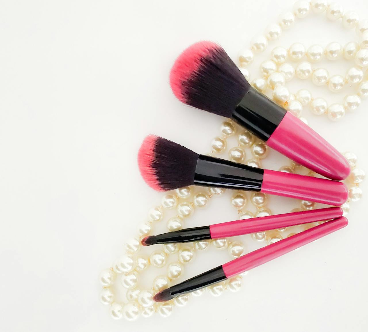 Home Pink and black makeup brushes arranged on pearl necklace for elegant look.